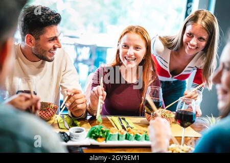 Des amis heureux mangeant avec des baguettes au restaurant sushi - concept de style de vie de nourriture et de boissons avec des jeunes s'amuser ensemble au bar fusion Banque D'Images