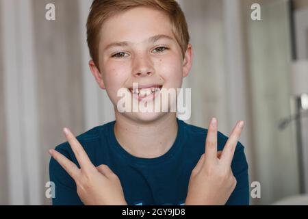 concept de geste, de triomphe, d'enfance, de mode et de personnes - un garçon souriant heureux dans un t-shirt bleu montrant la paix ou la victoire signe main sur fond clair Banque D'Images