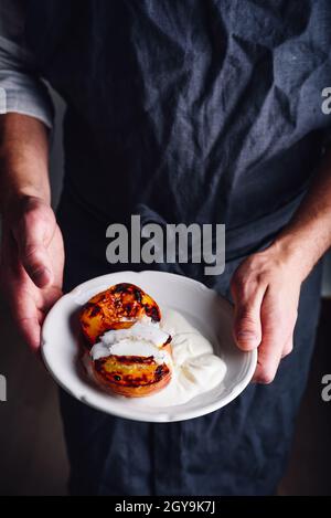 Assiette avec pêches cuites au miel et crème fouettée dans les mains des chefs Banque D'Images