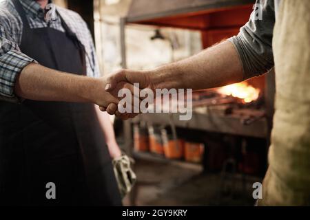 Gros plan de deux travailleurs se tenant et se serrant la main pendant leur travail en atelier Banque D'Images