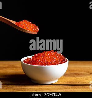 Caviar rouge dans une tasse en bois sur fond noir avec une cuillère.Une grande pile de caviar lumineux.Caviar frais et délicieux.Un lieu de publicité, logo, l Banque D'Images