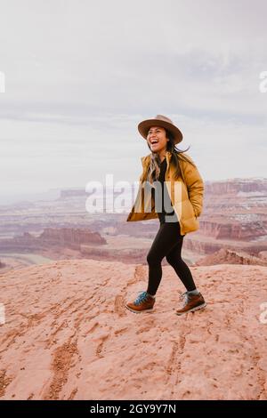 Une femme portant un chapeau à bord rit tout en faisant de la randonnée au-dessus du canyon du désert Banque D'Images