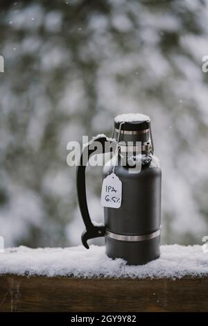 Un growler rempli de bière froide est assis sur une rambarde en bois enneigée à l'extérieur Banque D'Images