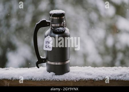 Un growler rempli de bière froide est assis sur une rambarde en bois enneigée à l'extérieur Banque D'Images