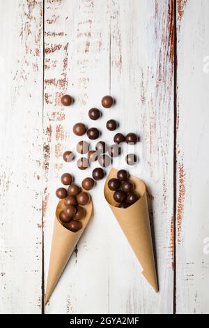 Différentes saveurs de pralines au chocolat dans des cônes en papier sur une table en bois. Banque D'Images