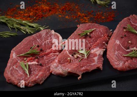 Trois morceaux de bifteck fin traditionnel coupés du filet sur planche à découper en bois avec de l'huile d'olive, du sel, du romarin et du poivre. Black Brut Angus Prim Banque D'Images