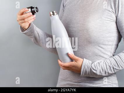 Gros plan d'une femme en t-shirt gris tenant une bouteille isotherme grise sur fond gris Banque D'Images