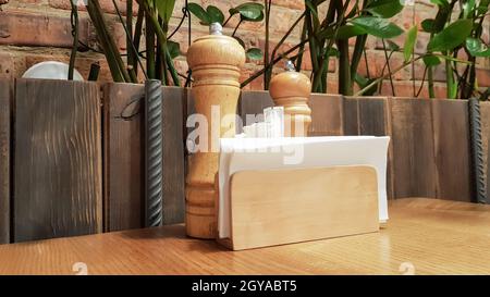 Une table dans un café ou un restaurant. Serviettes blanches dans un support en bois, sel et poivre sur une table en bois. Comptoir à pizza avec épices, serviettes et cure-dents. Banque D'Images