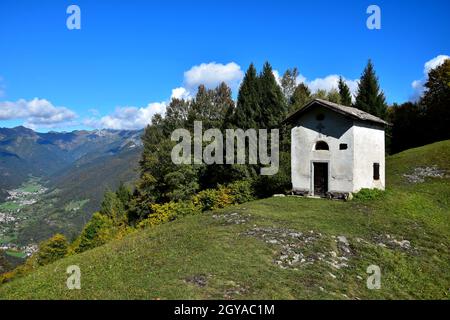 La petite chapelle de San Martino sur le mont Corno lors d'une belle journée d'automne claire. Sur la gauche quelques petites villes dans une vallée. Trentin, Italie. Banque D'Images