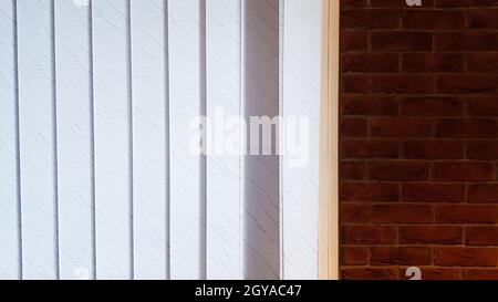 Grande fenêtre avec stores verticaux blancs ou gris, loft, mur de briques, intérieur industriel. Lumière du soleil provenant d'une fenêtre sur des murs en briques dans une pièce ou un bureau Banque D'Images