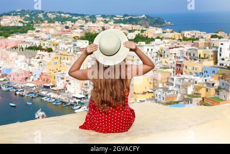 Belle jeune femme avec chapeau assis sur le mur et vue panoramique sur l'île de Procida, Naples, Italie. L'île de Procida est la capitale italienne Banque D'Images