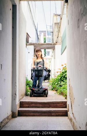 Une jeune femme sur un fauteuil roulant en scooter a l'air inquiète parce qu'elle ne peut pas descendre les marches Banque D'Images
