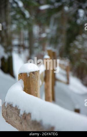 barre en bois barrière beige courbée route d'hiver dans la forêt. barres jaunes chapeau de neige Banque D'Images