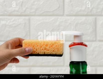 une femme tient la main d'une éponge de cuisine avec mousse blanche près du distributeur en plastique Banque D'Images