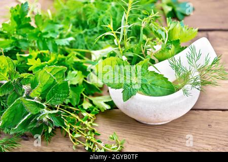 Feuilles et branches de menthe, d'aneth, d'estragon, de thym, de céleri et de persil dans un mortier en pierre avec un pilon et sur une table sur le fond d'un vieux W Banque D'Images