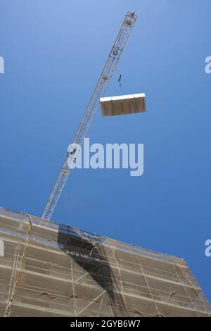 Grue avec charge de panneaux de cloison sèche sur le chantier de construction. Travailler sous un concept de charge suspendue Banque D'Images