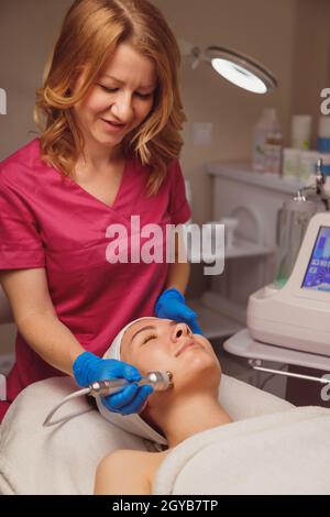 Une jeune femme se fait nettoyer la peau et se faire soigner au salon de beauté par micro-courants. Banque D'Images