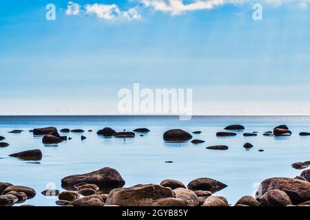 Pierres Boudders dans les vagues calmes de l'océan d'Azur contre un ciel bleu avec des nuages blancs. Banque D'Images