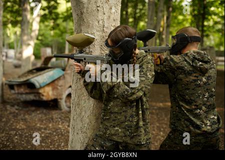 Hommes et guerriers famales dans des camouflages et des masques de tir avec des pistolets de paintball.Sport extrême avec arme pneumatique et peinture balles ou marqueurs, mili Banque D'Images