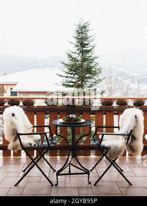 Balcon d'hiver avec table basse, chaises confortables couvertes de fourrure blanche et vue splendide sur les montagnes enneigées. Vacances d'hiver Banque D'Images