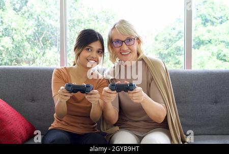 Happy mix peau famille vivant ensemble, fille asiatique et sa mère caucasienne adoptée jouer jeux de console dans le salon. Banque D'Images