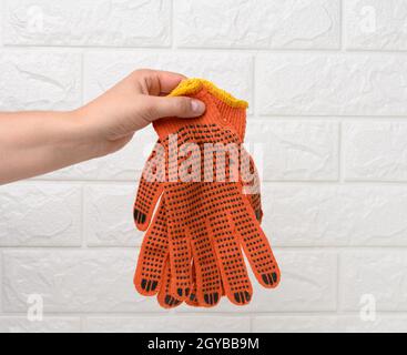 la main femelle tient des gants de travail en tissu orange sur un fond blanc. Vêtements de protection pour les travailleurs manuels, gros plan Banque D'Images