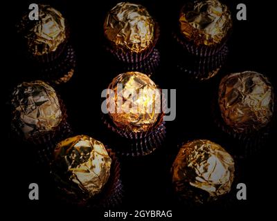 Bonbons au chocolat ronds dans un emballage doré sur fond noir. Bonbons ronds. Couleur dorée. Un cadeau de vacances. Anniversaire. Photo de nourriture. Mets sucrés. Happ Banque D'Images