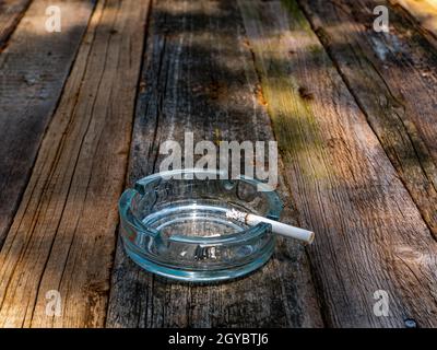 Cendrier en verre avec une cigarette sur une table en bois. Espace fumeurs. Une cigarette dans un cendrier. Table en bois. Produits du tabac. Mauvaise habitude. Nicotine. Santé Banque D'Images