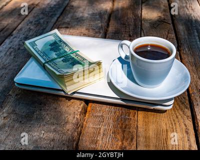 Une tasse de café et d'argent avec un ordinateur portable se trouve sur une table en bois. Boisson au café. Un paquet d'argent. Dollar américain. Tasse et soucoupe. Gagner de l'argent sur le Banque D'Images