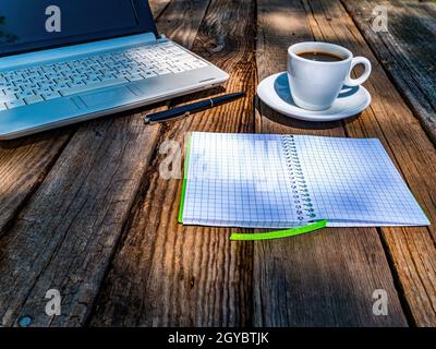 Le Bloc-notes avec une tasse de café et un ordinateur portable se trouve sur une table en bois. Boisson au café. Ordinateur portable. Stylo d'écriture. Tasse et soucoupe. Gagner de l'argent sur Internet. C Banque D'Images