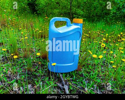 Un bidon en plastique bleu dans un jardin de junkyard dans l'herbe verte. Récipient pour produits chimiques. Couvercle jaune. Produits chimiques automobiles. Pollution de l'environnement. PLASTI Banque D'Images