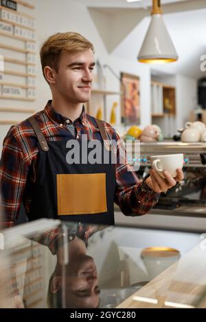 le baristas est souriant et le barisonne est à l'intérieur d'un tablier et tient une tasse de boisson chaude au café. le barista est heureux de travailler à la cafétéria Banque D'Images