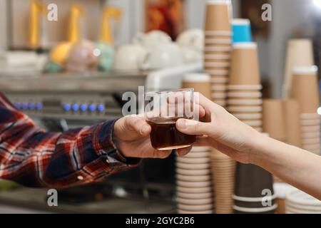 le barista professionnel en tablier donne un verre de café frais au client Banque D'Images