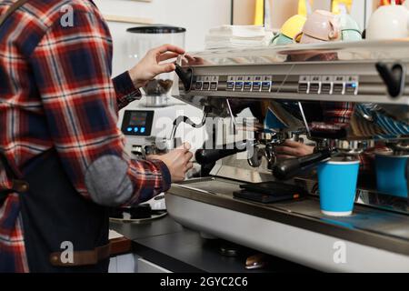 le barista professionnel en tablier verse du café frais dans une tasse à partir de la machine à café Banque D'Images