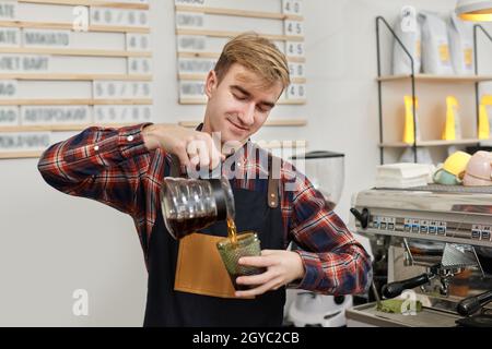 un barista professionnel en tablier verse du café frais dans une tasse Banque D'Images