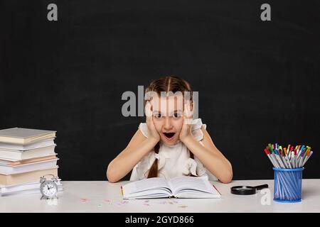 Enfant stressé fille lisant un livre dans la salle de classe sur fond de tableau noir. Retour à l'école. Banque D'Images