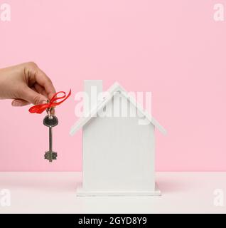 main tient les clés et la maison en bois sur un fond rose. Location, achat et vente de biens immobiliers. Services de realteur, réparation de bâtiments et entretien Banque D'Images