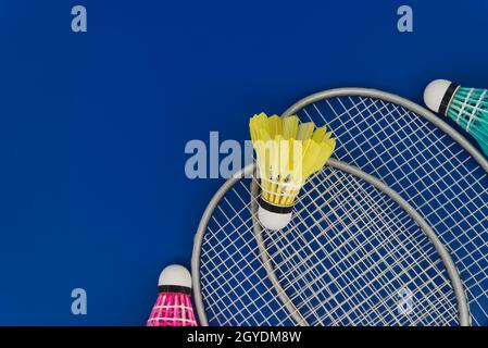 Badminton. Raquettes et volants à plumes colorés en bleu, jaune et rose sur fond bleu dans la vue de dessus avec espace de copie gratuit Banque D'Images