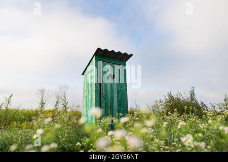 toilettes vintage. Une toilette extérieure rustique verte avec un coeur découpé sur la porte. Toilette dans un champ de fleurs Banque D'Images