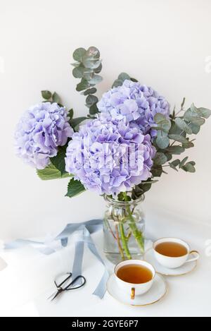 Deux tasses de thé noir dans une magnifique tasse blanche en porcelaine avec une coupe d'or. Magnifique bouquet d'hortensia violet sur la table. Concept de cérémonie du thé Banque D'Images