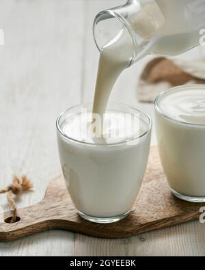 Verser du kéfir, du babeurre ou du yogourt avec des probiotiques.Yaourt provenant d'une bouteille en verre sur fond de bois blanc.Lait laitier fermenté à froid probiotique Banque D'Images