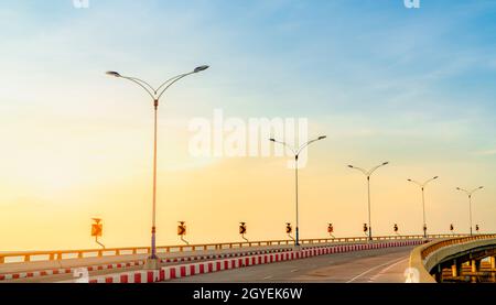 Route en béton avec courbe et panneau de circulation sur le sentier au bord de la mer au coucher du soleil. Panneau solaire d'énergie sur la courbe jaune du panneau de signalisation. Trajet sur route activé Banque D'Images