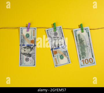 Une centaine de billets de dollars américains pendent sur une corde avec des épingles à linge, fond jaune. Concept de blanchiment d'argent Banque D'Images