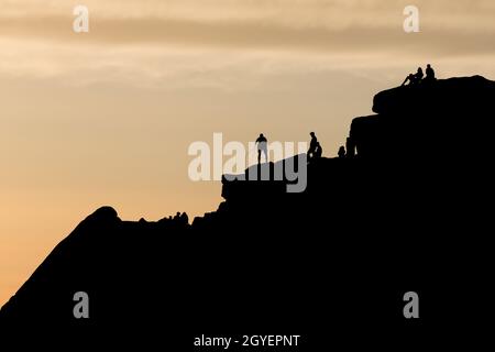 Une scène de silhouette spectaculaire en tant que grimpeur trie ses cordes au sommet d'une formation de roche frappante. D'autres personnes apprécient le coucher du soleil et la nature sauvage éloignée. Banque D'Images