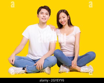 Jeune couple souriant à la caméra tandis que la femme mettant sa main sur l'épaule mâle.isolé sur fond jaune. Banque D'Images