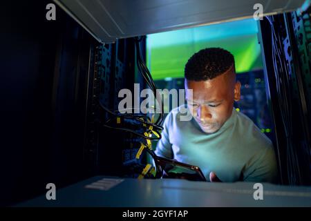 Un technicien informatique afro-américain utilisant une tablette et travaillant dans une salle de serveurs Banque D'Images