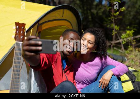 Heureux couple divers assis dans la tente et prenant le selfie dans la campagne Banque D'Images