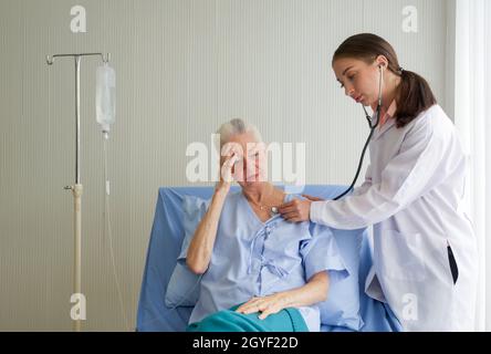 Patiente et médecin senior. Le jeune médecin utilise un stéthoscope pour vérifier le rythme cardiaque des patients âgés souffrant de maux de tête vertigineux. Banque D'Images