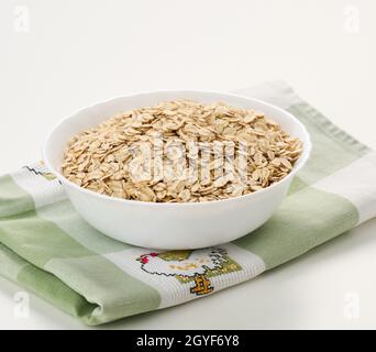 Flocons d'avoine crus dans une assiette en céramique blanche sur une table blanche, petit déjeuner Banque D'Images