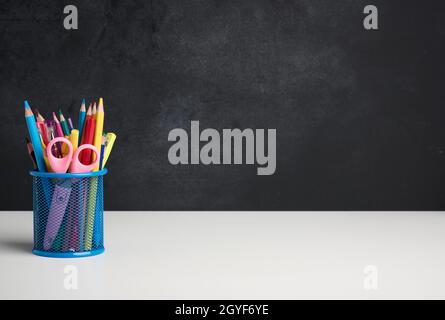 verre métallique avec stylos, crayons et stylos-feutres et ciseaux sur le fond d'un tableau noir vide, table blanche, espace de copie Banque D'Images